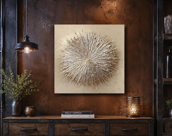 May include: A square wall art piece featuring a textured, three-dimensional gold and metallic sunburst design centered on a light beige background. The artwork displays radiating lines and raised elements that create a starburst effect with depth.