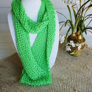 May include: A bright green knitted scarf, made with a simple stitch pattern, is displayed on a white mannequin. The scarf is folded in half and draped around the mannequin's neck.