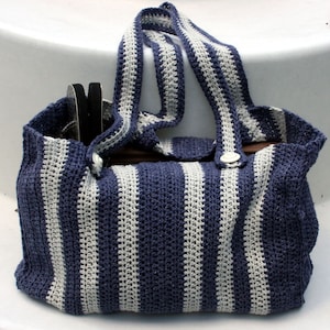 May include: A striped crocheted tote bag with blue and white stripes. The bag has a single button closure and two long straps.