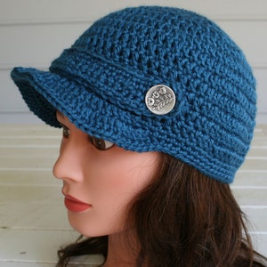 A blue summer cap with a stylish visor.  Crocheted with a Soft ShimmeryTeal Blue Yarn and finished off with a buttoned brim.