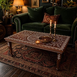 May include: A rectangular wooden coffee table featuring intricate white floral and geometric inlay patterns across its surface and legs. The table holds two tall brass candlesticks with lit white candles and a shallow bowl filled with nuts.