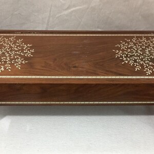 Op de afbeelding: Een houten tafel met een bruine afwerking en ingelegde witte bloemmotieven op de bovenkant. De tafel heeft vier poten en een rechthoekige vorm.