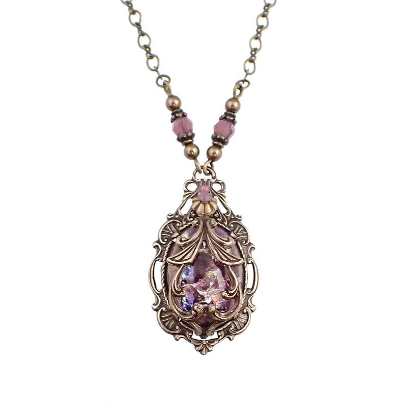 May include: A delicate gold necklace with a pink and purple iridescent glass pendant set in an ornate filigree frame.