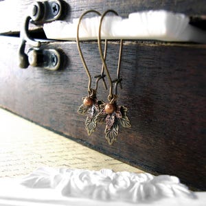 Peut inclure: Une paire de boucles d'oreilles en forme de feuilles de bronze avec des perles en cuivre suspendues à un crochet.