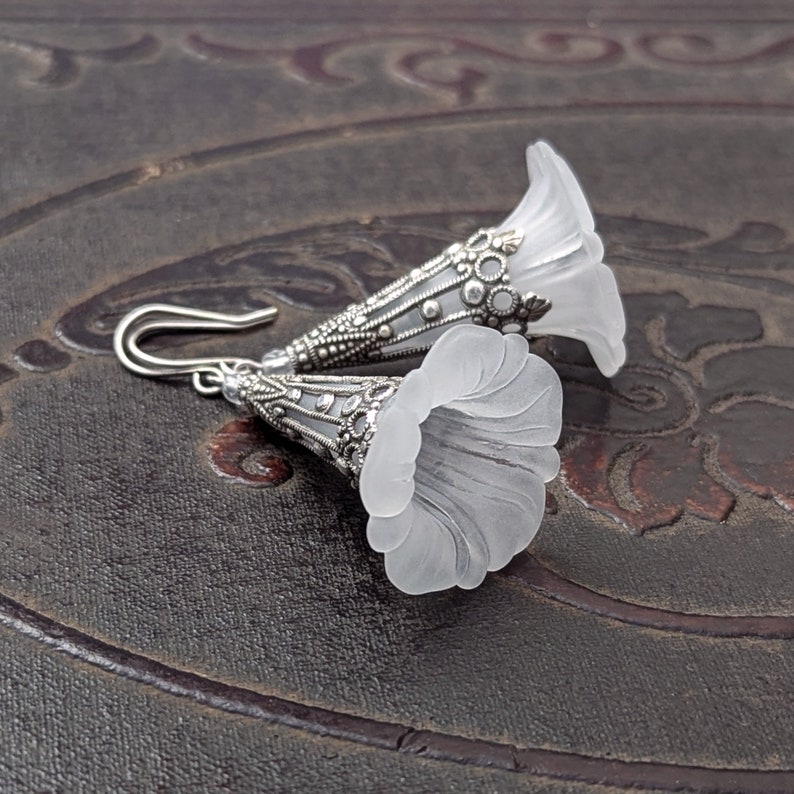 Lucite flower earrings in frosted white with antiqued silver filigree cones photographed on a vintage brown background