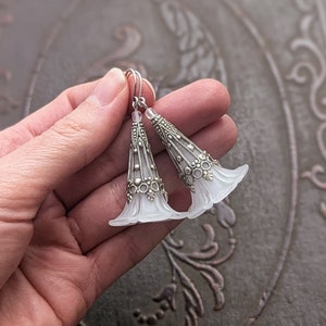 Lucite flower earrings in frosted white with antiqued silver filigree cones photographed on a vintage brown background