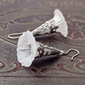 Lucite flower earrings in frosted white with antiqued silver filigree cones photographed on a vintage brown background
