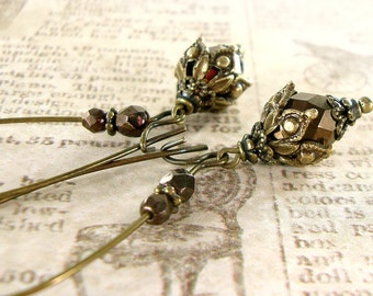 May include: A pair of gold-toned earrings with a dark brown faceted glass bead and a detailed metal design. The earrings are hanging from a thin wire.