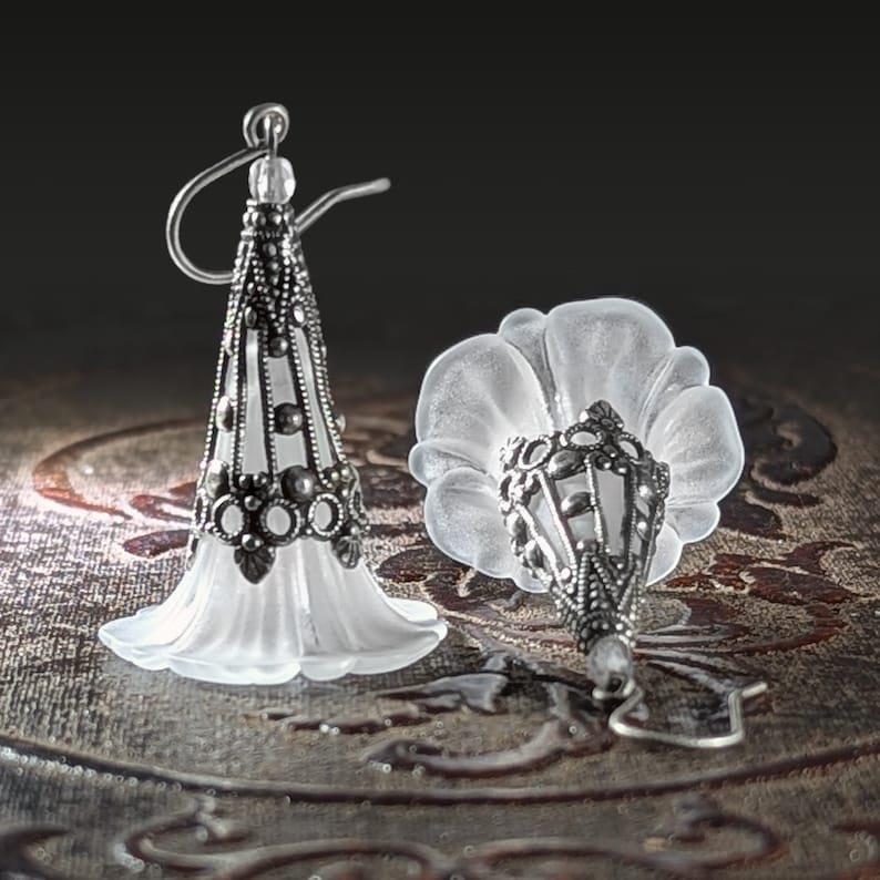 Lucite flower earrings in frosted white with antiqued silver filigree cones photographed on a vintage brown background