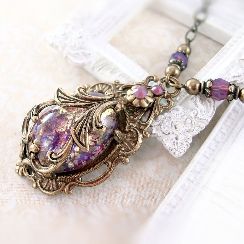 May include: A purple and gold iridescent glass pendant with an ornate brass frame. The pendant is hanging from a chain with purple glass beads.