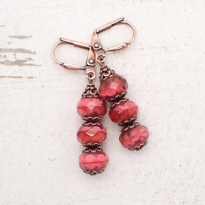 May include: A pair of copper dangle earrings with three red faceted glass beads on each earring.