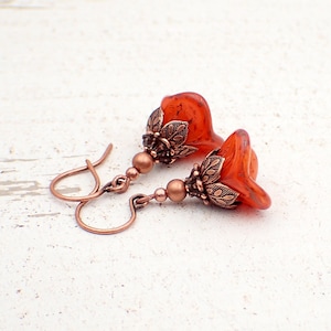 May include: A pair of copper earrings with orange glass flower-shaped beads. The earrings have a delicate, vintage-inspired design.