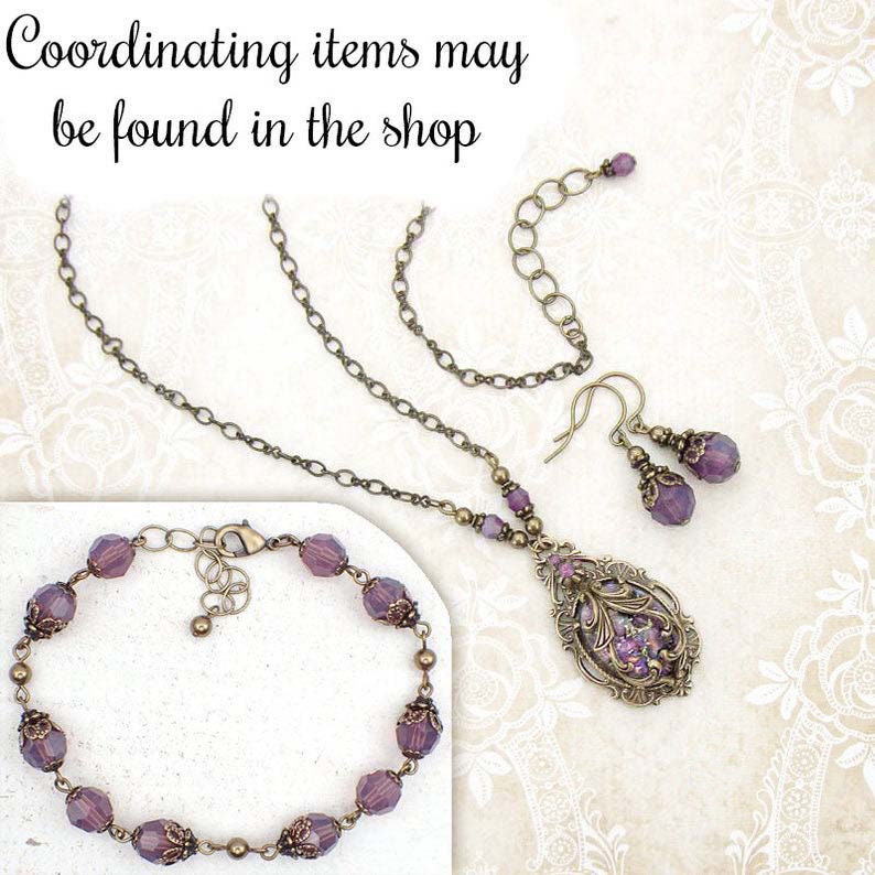 May include: A set of purple and bronze jewelry featuring a necklace, bracelet, and earrings. The necklace has a large, ornate pendant with a purple stone. The bracelet is made of small purple beads and bronze chain. The earrings are dangle earrings with purple stones.