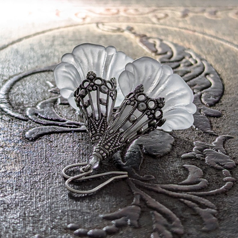 Lucite flower earrings in frosted white with antiqued silver filigree cones photographed on a vintage brown background