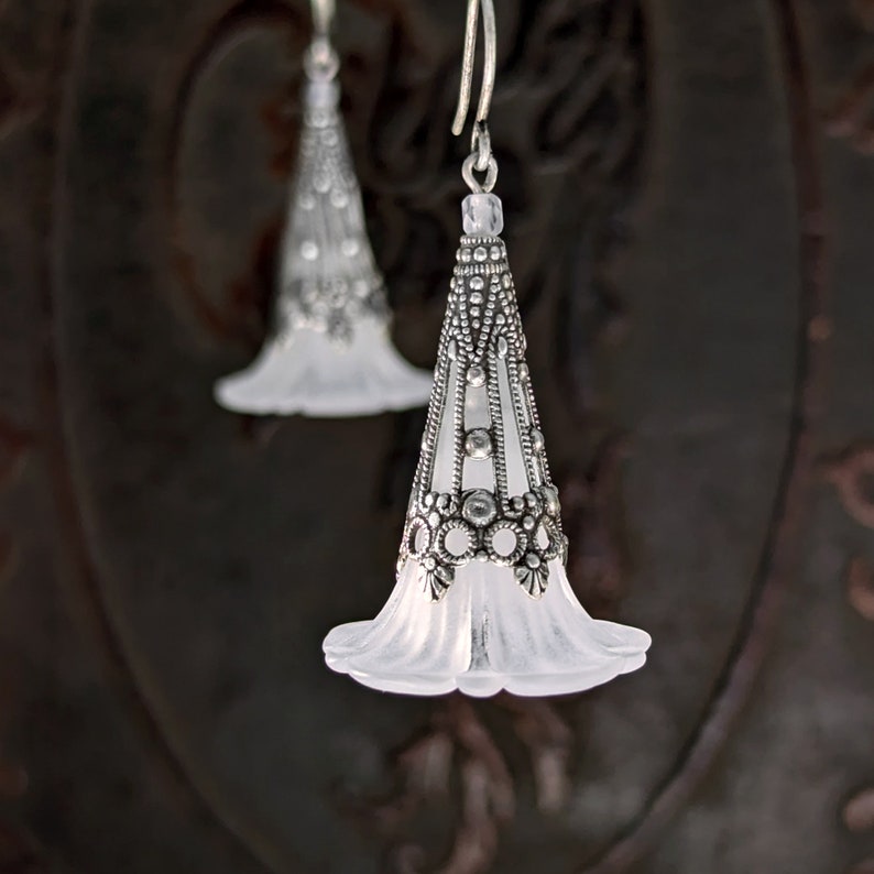 Lucite flower earrings in frosted white with antiqued silver filigree cones photographed on a vintage brown background