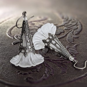 Lucite flower earrings in frosted white with antiqued silver filigree cones photographed on a vintage brown background