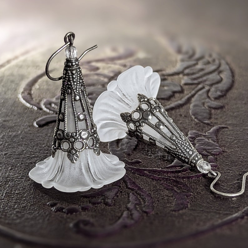 Lucite flower earrings in frosted white with antiqued silver filigree cones photographed on a vintage brown background