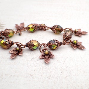 May include: A copper bracelet with green iridescent glass beads and copper leaf charms. The bracelet is made with wire wrapped beads and has a delicate, feminine style.