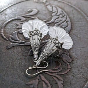 Lucite flower earrings in frosted white with antiqued silver filigree cones photographed on a vintage brown background