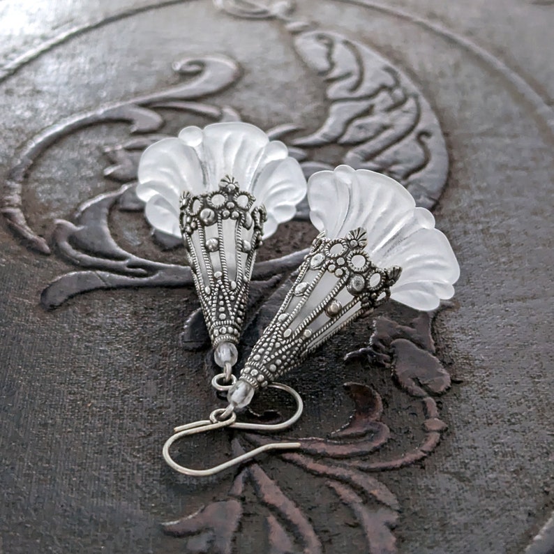 Lucite flower earrings in frosted white with antiqued silver filigree cones photographed on a vintage brown background