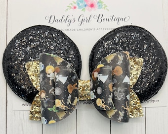 Puede incluir: Lazos para el pelo con forma de orejas de ratón con purpurina negra, con un lazo dorado y un estampado temático de Star Wars. Los lazos están sujetos a una tarjeta blanca con el texto "Daddy's Girl Boutique".