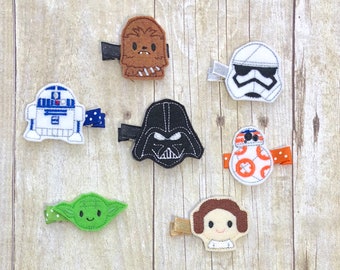 Könnte beinhalten: Eine Sammlung von Haarspangen mit Star Wars-Charakteren. Die Spangen zeigen Charaktere wie Chewbacca, Darth Vader, R2-D2, einen Sturmtruppler, BB-8, Yoda und Prinzessin Leia. Jede Spange ist aus Filz gefertigt und hat einen kleinen Metallclip.