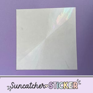 May include: A square, white suncatcher sticker with iridescent rainbow highlights. The sticker is on a purple background. The text "Suncatcher STICKER" is at the bottom of the image.