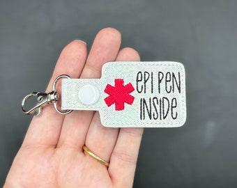 May include: White keychain with a red medical symbol and the text "epi pen inside".