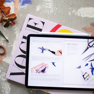 Pu&ograve; includere: Un tablet che mostra un tutorial di artigianato su come realizzare un uccello usando colla e pinzette. Il tutorial include immagini dei passaggi coinvolti e testo sulla colla. Il tablet &egrave; sopra una rivista rosa con la parola "Vogue" stampata su di essa.