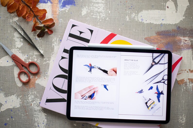 Pu&ograve; includere: Un tablet che mostra un tutorial di artigianato su come realizzare un uccello usando colla e pinzette. Il tutorial include immagini dei passaggi coinvolti e testo sulla colla. Il tablet &egrave; sopra una rivista rosa con la parola "Vogue" stampata su di essa.
