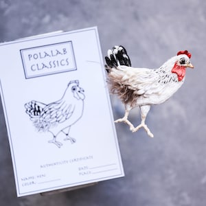 May include: A white and black chicken figurine with a red comb and wattle. The figurine is standing on a white card with the text "POLALAB CLASSICS" and an authenticity certificate.