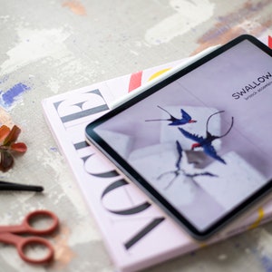 Pu&ograve; includere: Un tablet con una rivista sotto. Lo schermo del tablet mostra una copertina di rivista con il titolo "SWALLOW" e le parole "brook & street" in un carattere pi&ugrave; piccolo. La copertina della rivista presenta uno sfondo viola chiaro con un design di uccelli blu e bianchi.