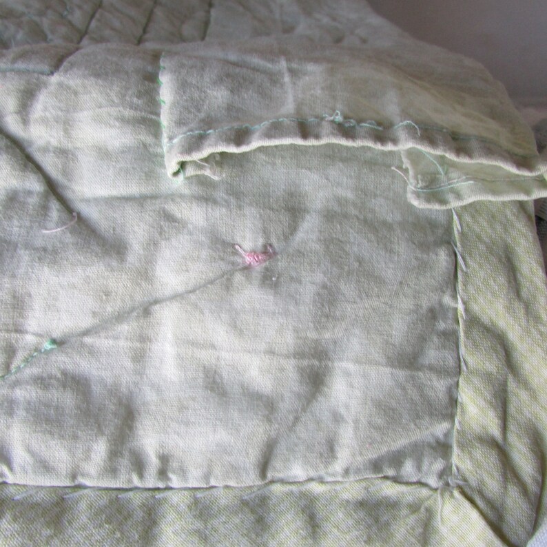 May include: Close-up of a light green quilt with a pink thread detail. The quilt is made of a soft, textured fabric and has a simple, elegant design.