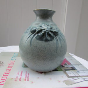 May include: A light blue ceramic vase with a raised floral design. The vase has a round body and a narrow neck.