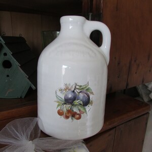 May include: White ceramic pitcher with a handle, featuring a painted design of plums and cherries on a branch.