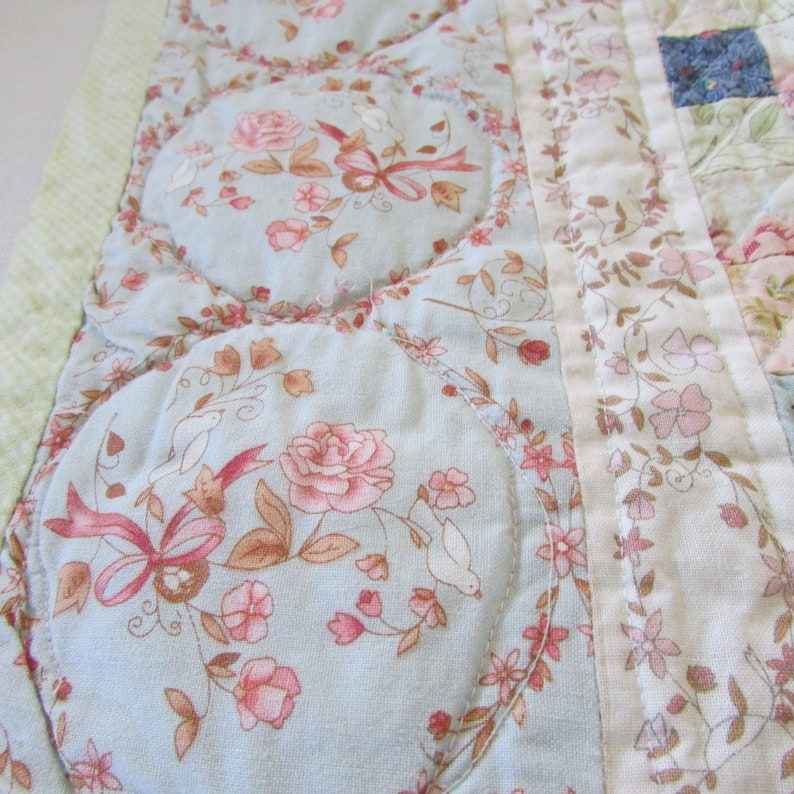 May include: A blue and white floral quilt with a quilted design. The quilt features a variety of floral patterns and colors, including pink, white, and green.
