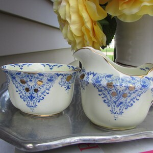 May include: A white creamer and sugar bowl set with blue and gold floral designs. The set is on a silver tray.