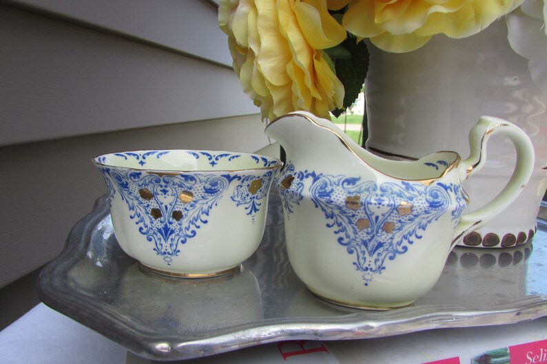 May include: A white creamer and sugar bowl set with blue and gold floral designs. The set is on a silver tray.