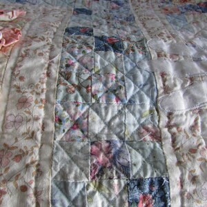 May include: A patchwork quilt with a variety of floral patterns in shades of pink, blue, and white. The quilt is quilted in a diamond pattern.