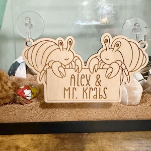 May include: Wooden sign featuring two cartoon crabs holding a sign that reads "Alex & Mr. Krabs." The crabs are light brown with detailed etched lines. The sign is designed to be hung with two suction cups.