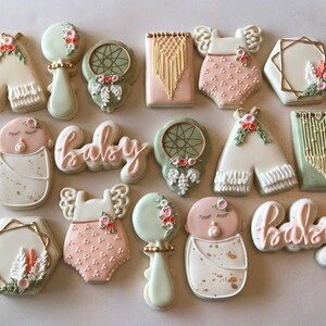 May include: A collection of 14 decorated sugar cookies with a bohemian theme. The cookies feature images of a baby, a teepee, a dreamcatcher, a rattle, and the word "baby".