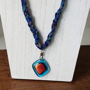 May include: A blue and purple fabric necklace with a blue and orange glass pendant.
