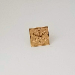 May include: A gold-colored square-shaped wax seal with a snowflake design.