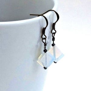 May include: A pair of silver earrings with iridescent white square-shaped stones hanging from the bottom. The earrings have black beads on the wire.