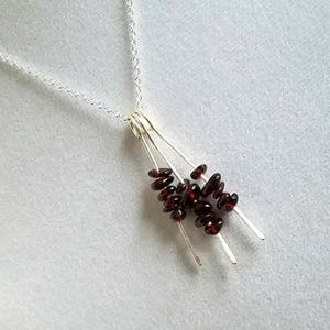 May include: A silver necklace with a pendant featuring multiple strands of small, dark red garnet beads.