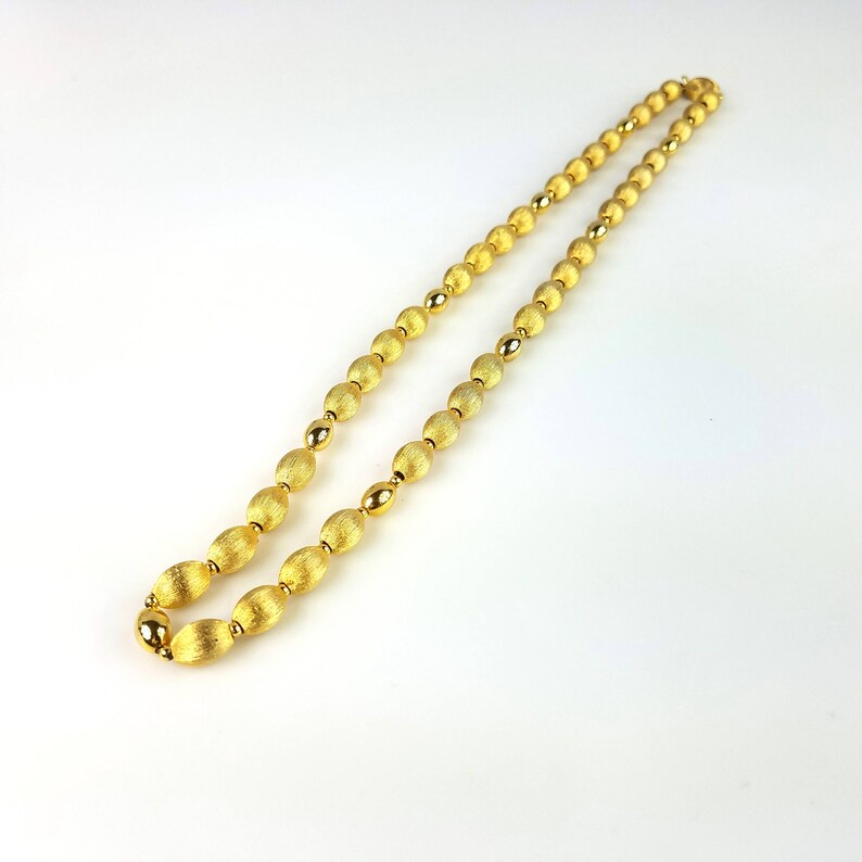 Op de afbeelding: Een gouden ketting gemaakt van ovale kralen. De kralen hebben een getextureerd oppervlak.