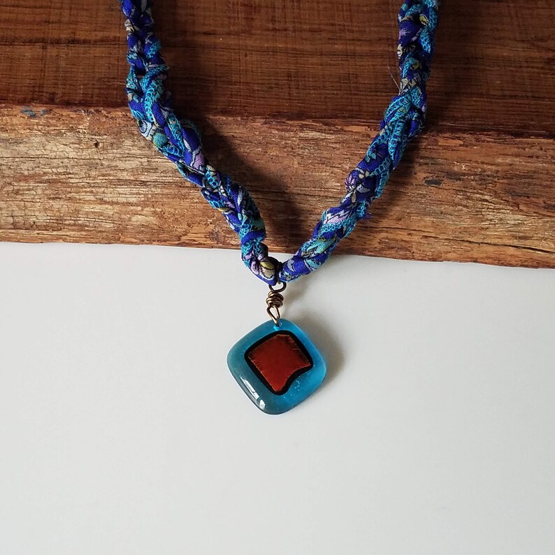 May include: A blue and white fabric necklace with a blue and red glass pendant.