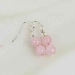 May include: A pair of silver dangle earrings with three pink faceted gemstone beads.