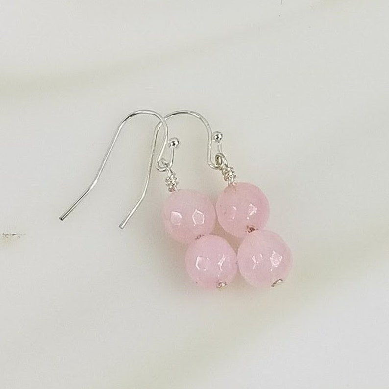 May include: A pair of silver dangle earrings with three pink faceted gemstone beads.