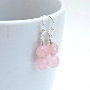 May include: A pair of silver dangle earrings with two pink faceted beads on each earring.